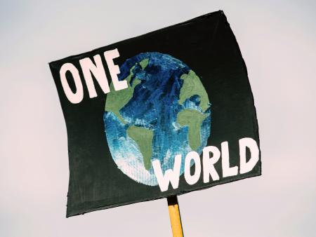 A protest sign with a picture of the Earth and the slogan 'One World'